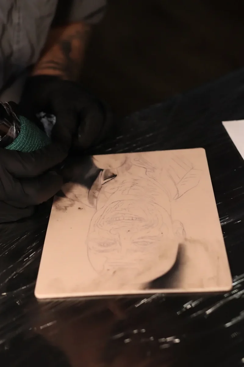 Gloved artist working on a portrait stencil on a FAKED SKIN tattoo practice pad