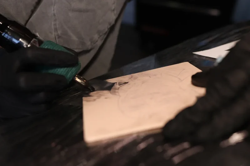 Artist using a tattoo machine on a portrait stencil on a Faked Skin practice pad