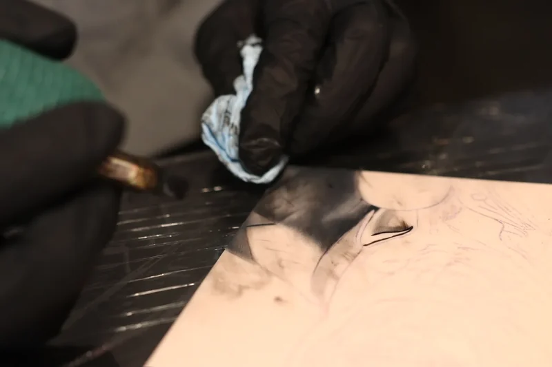 Artist wiping black ink from a shaded portrait area on a practice pad